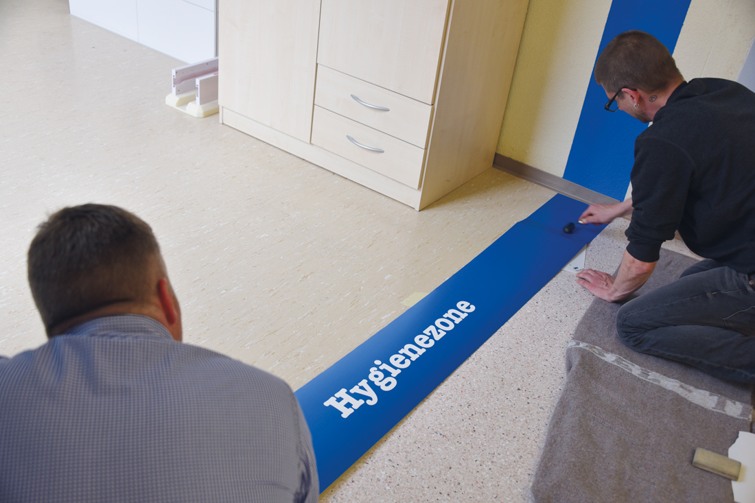 Blaue Signalisation fuer die Hygienezone wird als Streifen ueber die Wand und den Boden gezogen