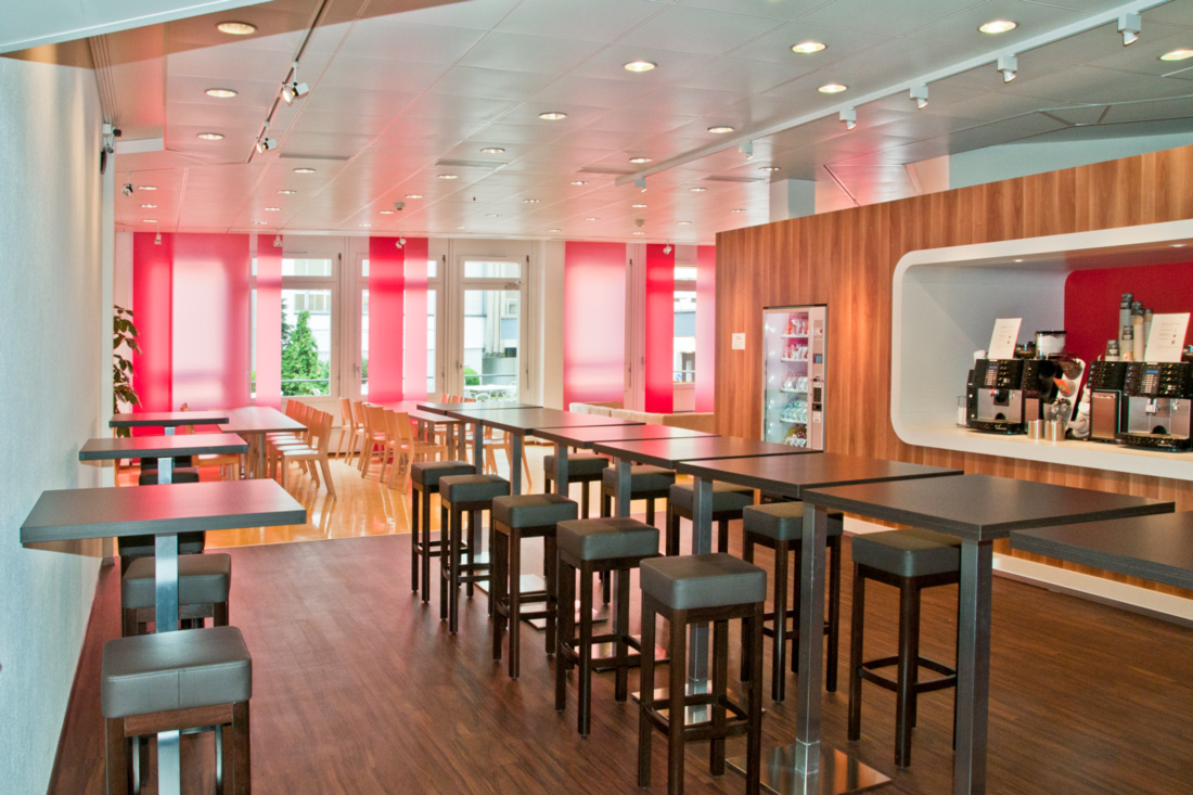 Neugestaltung Cafeteria: Frische warme Farben, Bartisch und bedruckte Hängepanelen im Rotton