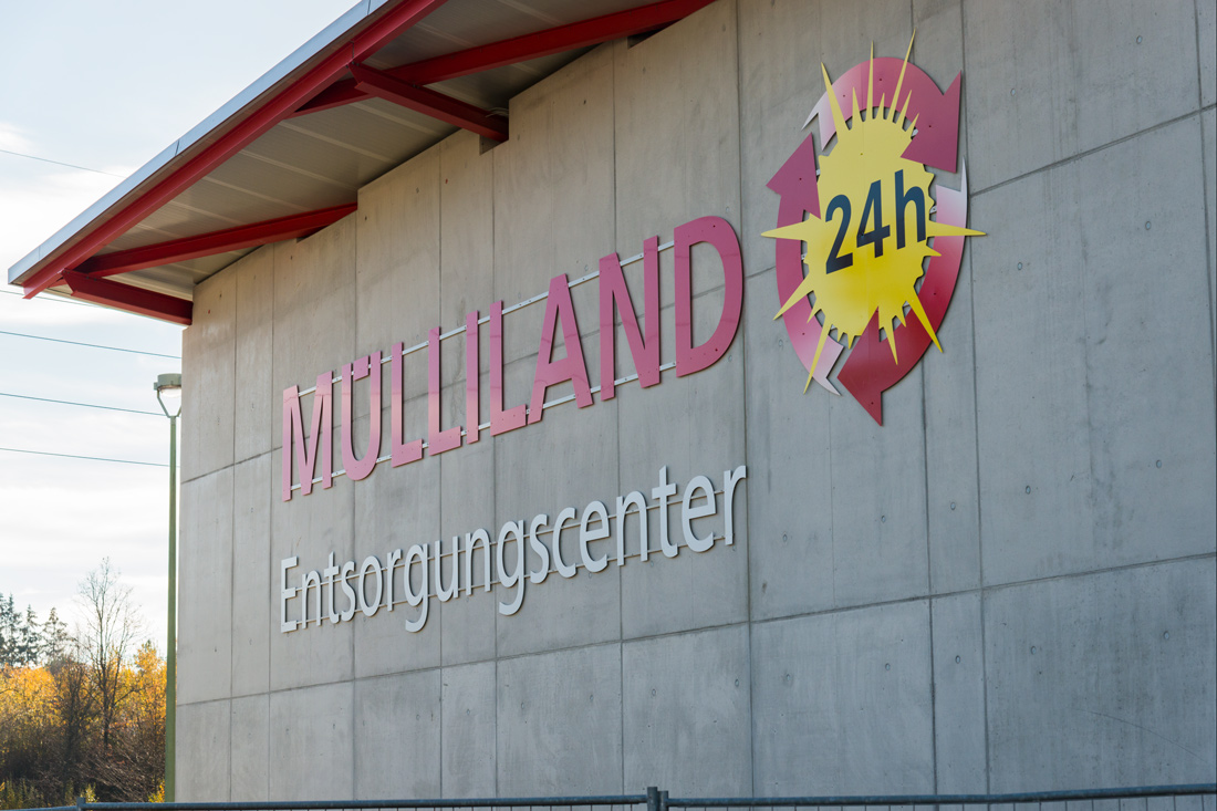 Rote Leuchtschrift an der Fassade Muelliland, Entsorgungscenter mit leuchtender Sonne mit natuerlichem Lichteffekt