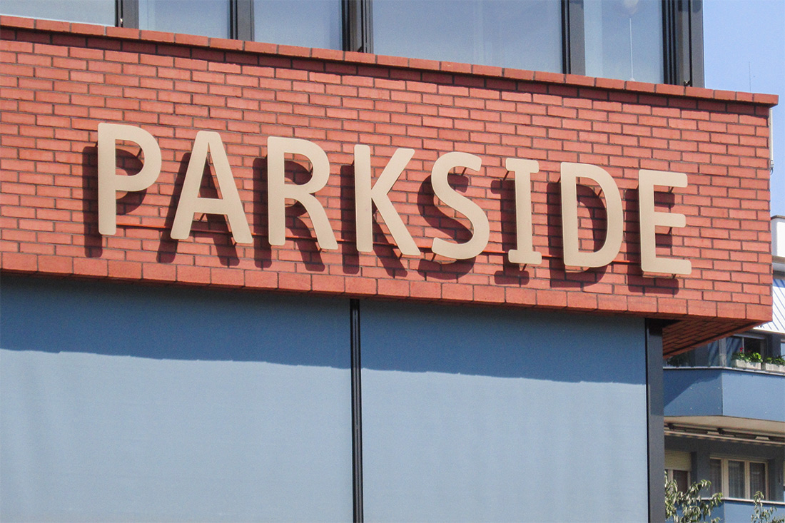 Leuchterbung Parkside mit Fassadenbeschriftung: Einzelne hinterleuchtete Buchstaben auf roher Backsteinwand montiert.